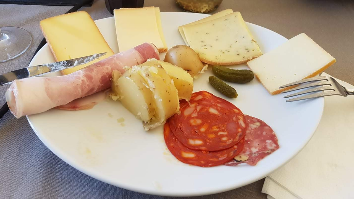 Assiette de raclette avec différents fromages, des pommes de terre, des cornichons et de la charcuterie